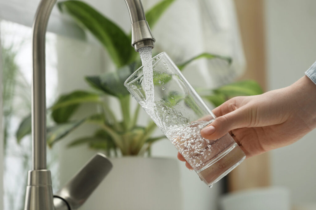person filling up a glass of water at a sink