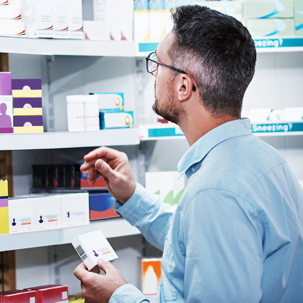 A man in glasses holding a product box and looking at shelves in a store.