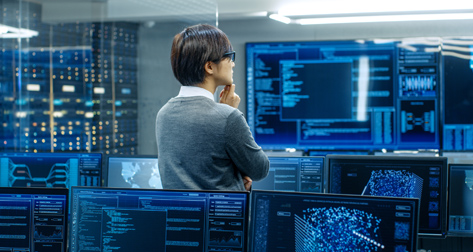 A person in a control room looking at multiple computer screens displaying data.