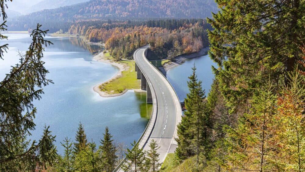 Epic curved bridge in Bavaria seen from above in front of a lake and mountain range while autumn - horizontal wide shot.