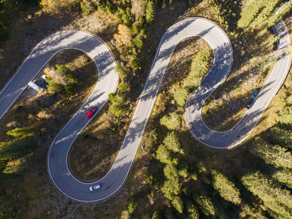 Aerial view of a road winding through a dense green forest in dolomites national park