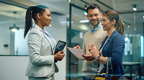 Three business professionals, two women and one man, discussing documents in a modern office.
