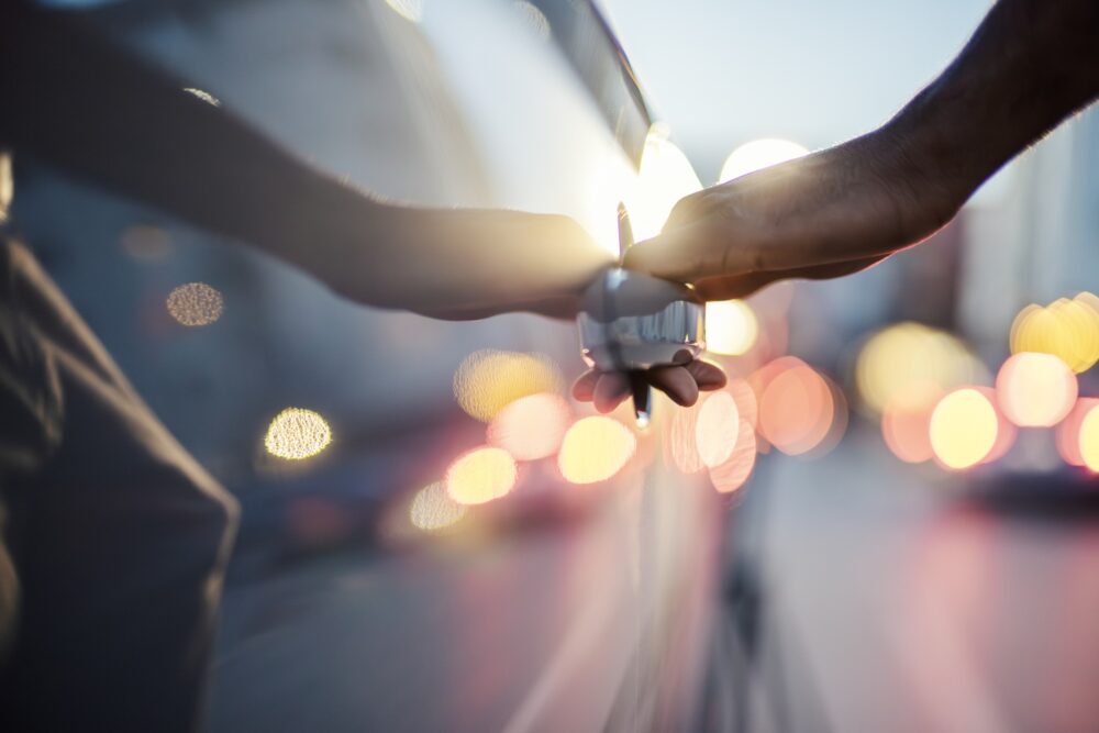 Human hand opening a car door with abstract city lights creating a colorful bokeh background