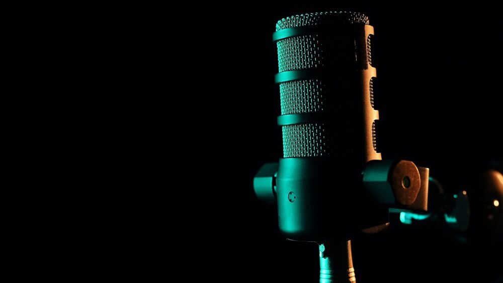 A professional studio microphone illuminated by atmospheric green lighting against a dark background. A sleek and modern setup for podcasting